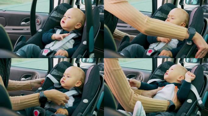 特写男婴坐在车内的婴儿汽车座椅上。妈妈打开门，放下把手，解开安全带，小心地把婴儿从座位上拿下来。慢动