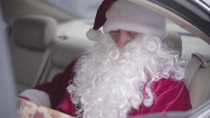 大胡子的圣诞老人从车窗给无法辨认的孩子礼物。老圣诞老人坐在汽车后座上。圣诞节，节日，礼物概念