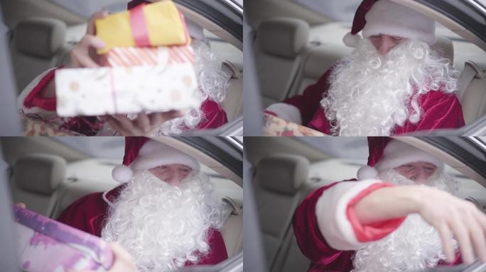 大胡子的圣诞老人从车窗给无法辨认的孩子礼物。老圣诞老人坐在汽车后座上。圣诞节，节日，礼物概念