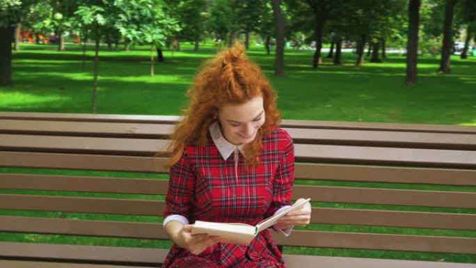 在绿色公园读有趣的书的漂亮女孩