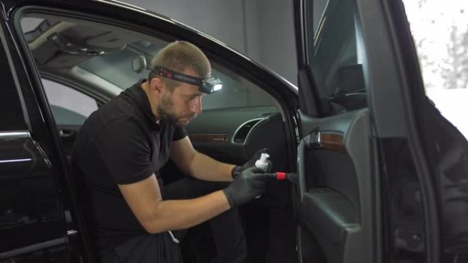 该男子用抗菌剂处理汽车内部，用刷子清洁车门的裂缝，详细清洁汽车内部