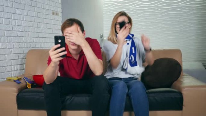 快乐女人运动迷赢得赌注并观看智能手机。失望的男子体育迷因失去一支球队而沮丧。概念: 体育、博彩。用赌