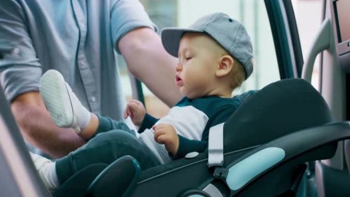 车内摄像头。特写婴儿汽车座椅。门打开，男婴出现了，由他年轻的大胡子父亲抱着，父亲将婴儿放在婴儿汽车安