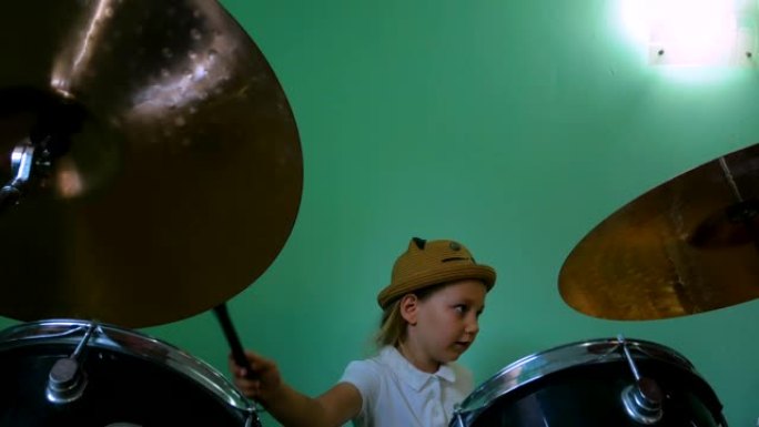 在音乐学校学习鼓的孩子。黑色鼓包。绿色墙壁背景上的鼓刷训练小音乐家鼓手。戴着帽子的金发小女孩在课上玩