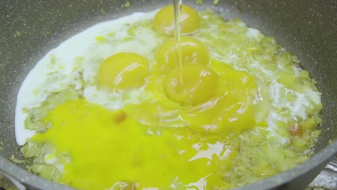 慢动作视频，将鸡蛋分解到装有洋葱，香料和调味料的煎锅中。烹饪炒鸡蛋，菜肉馅煎蛋饼，煎蛋或煎蛋。准备减