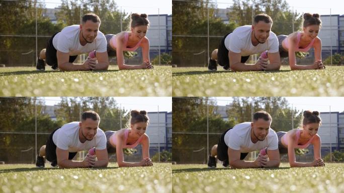 一个男人和一个女孩在体育场的草地上做木板运动的特写镜头。
