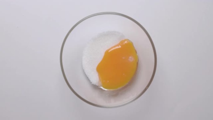 从装有糖的玻璃碗上方的俯视图。鸡蛋黄从勺子里掉到碗里。