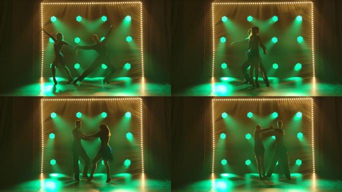 一对专业舞者表演拉丁美洲舞厅舞伦巴、恰恰恰舞、桑巴舞的元素。剪影夫妇在绿光的黑暗工作室里热情地跳舞。