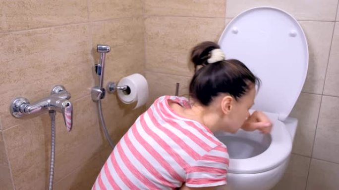 怀孕的年轻疲倦的女人正在厕所里呕吐，坐在家里的地板上，向后看。
