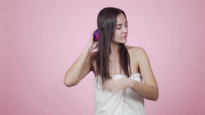 女子淋浴后用梳子梳湿头发，孤立在粉红色的背景