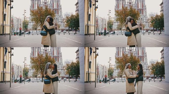 穿着休闲外套的亚洲成熟妈妈和成年女儿在城市广场见面，微笑，亲吻，拥抱彼此