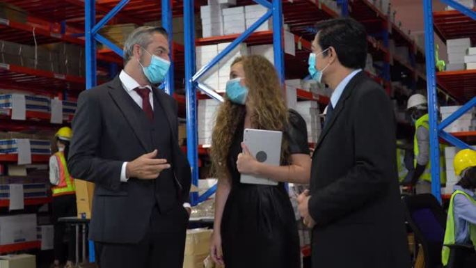 执行业务人员和秘书女士戴着面部防护医用口罩与大型仓库的亚洲仓库经理交谈。业主参观工厂并与主管一起检查
