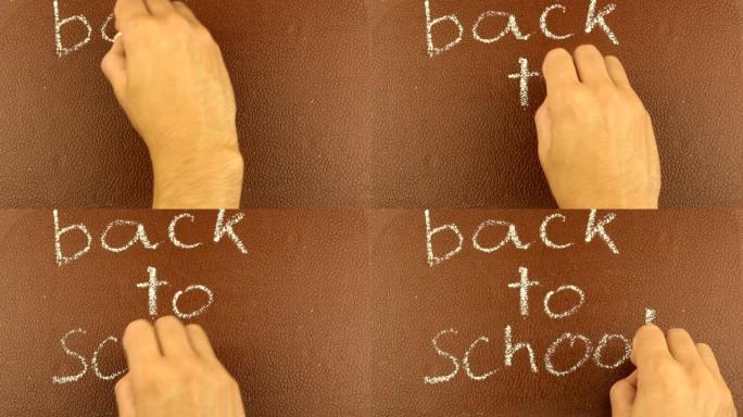 一只男性手的特写镜头用粉笔在棕色黑板上写回学校。一个人用粉笔在棕色板上写回学校。