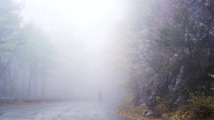 孤独的人在神秘的雾中行走。穿着红色夹克的男子在山上迷失的手机上寻找信号