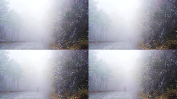 孤独的人在神秘的雾中行走。穿着红色夹克的男子在山上迷失的手机上寻找信号