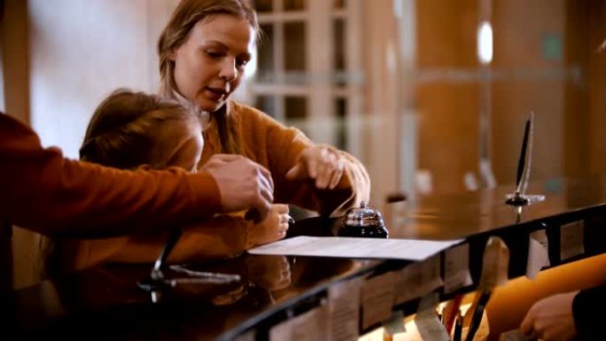一家在豪华酒店登记入住的家庭-一个小女孩在玩铅笔之前，她的母亲从她那里拿走了铅笔在文件上签名