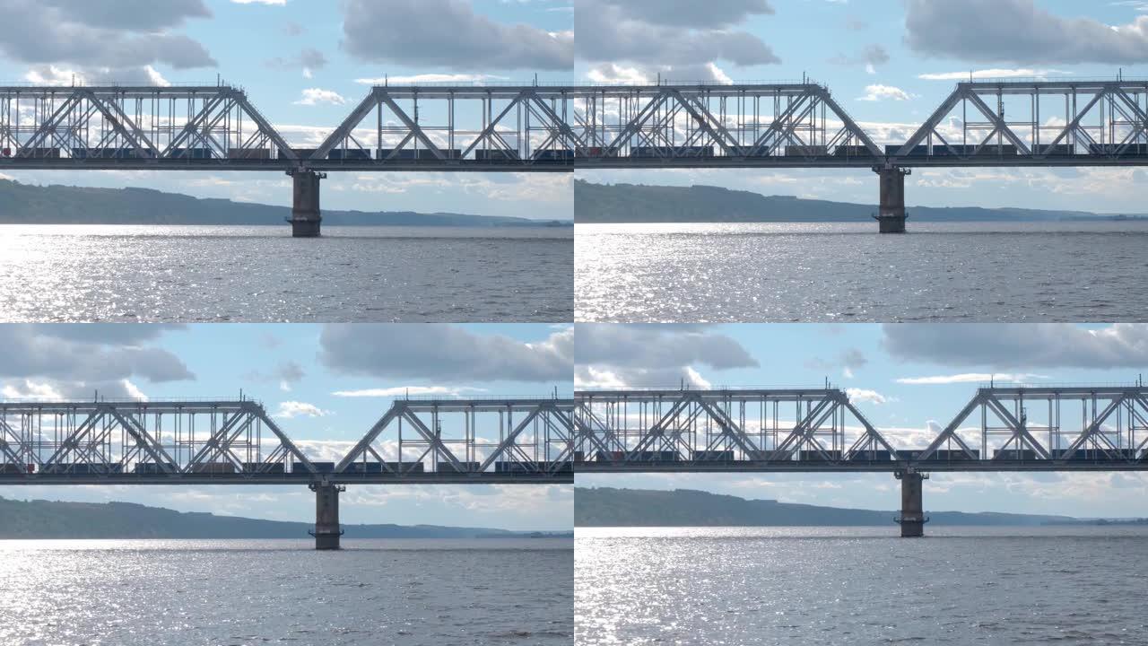 一列长长的货运火车在宽阔的河上过桥。从平行航线上航行的渡轮上拍摄。
