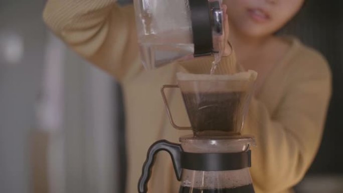 年轻女子用过滤器将水倒在咖啡粉上。