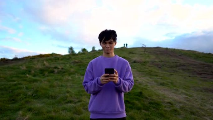 多莉走出年轻千禧一代亚洲男子站在户外自然环境中使用智能手机发短信的肖像 -- 智能手机成瘾