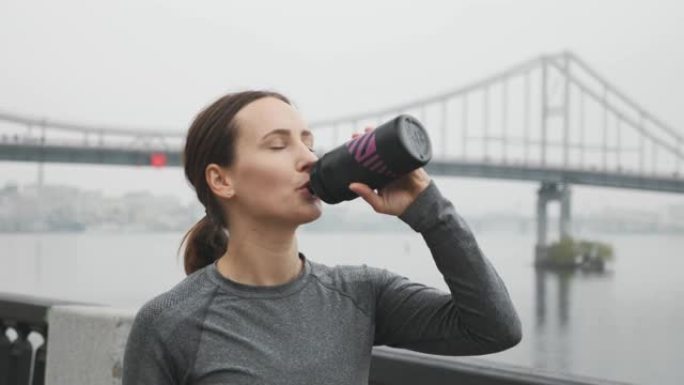 年轻漂亮的运动女运动员穿着保暖内衣，跑步训练后喝等渗。女跑步者在户外锻炼后从瓶子里喝水