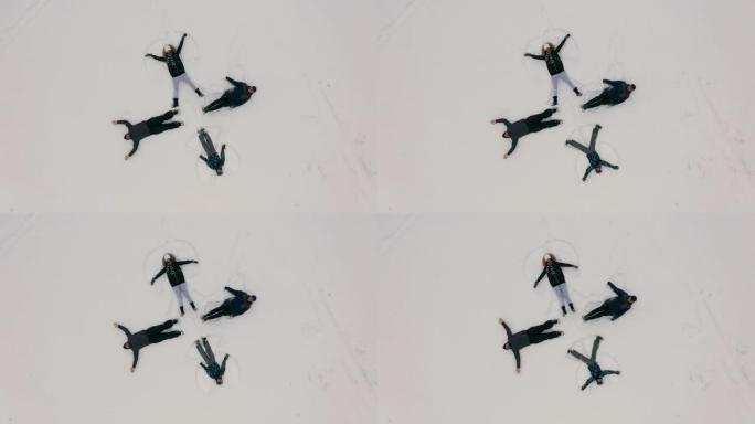 鸟瞰图。一群年轻人以十字架的形式描绘了躺在新鲜雪地上的雪天使。四个冬天的天使快乐而充满活力，雪花飞溅