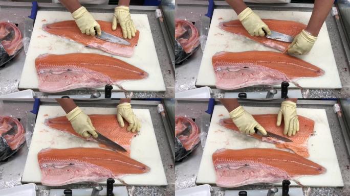 日本专业厨师在手套切割，切片新鲜的生红三文鱼。双手用刀特写。鱼工厂，商店，生产，商业厨房。地中海饮食