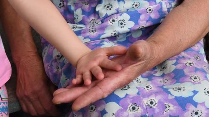 老皱手触摸和拍拍孩子柔软的手。孙子和祖母的特写手