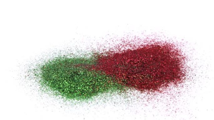 飘落的红色和绿色闪光灰尘。红色和绿色的火花落在白色背景上。圣诞闪光灰尘