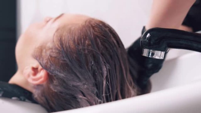 美发师用水洗一个年轻漂亮的客户的头。