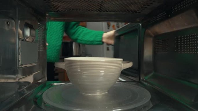 女人的手在微波炉里放一个陶瓷碗，里面放一些食物