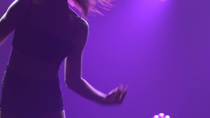 轻烈的性感女舞者旋转跳跃，在带有紫色灯光的黑暗工作室里轻蔑地跳舞。特写细长身体的轮廓。慢动作