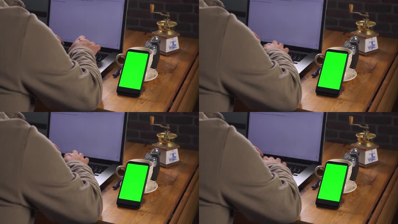 带有绿色屏幕的模型，用于跟踪特写。成年白人男子坐在木桌旁，在笔记本电脑上输入文字。附近有一部带触摸屏