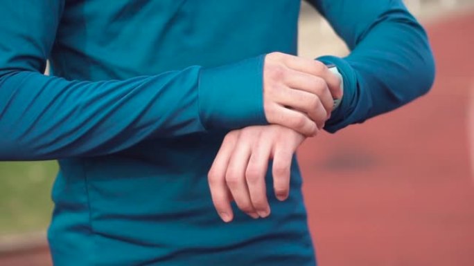 特写镜头，男子赛跑者在体育场看智能手表。年轻运动员在跑道上检查智能手表的结果。