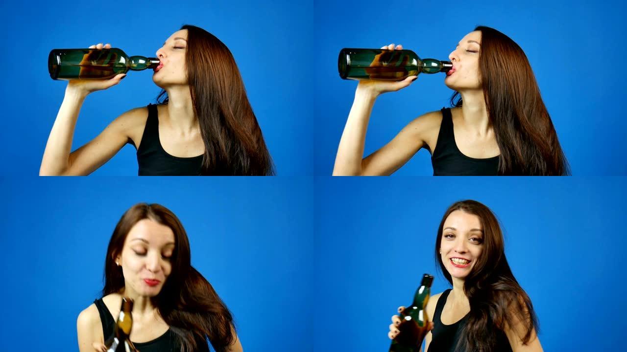 年轻的黑发女人正在工作室里喝蓝色背景的深绿色瓶子里的葡萄酒