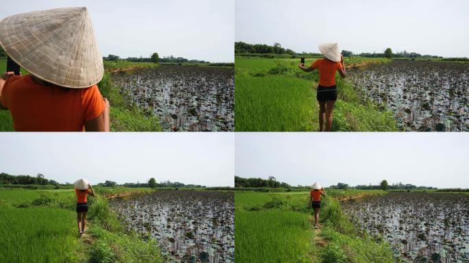 穿着越南锥形帽子的年轻女子在农场里散步，拍摄自拍视频。