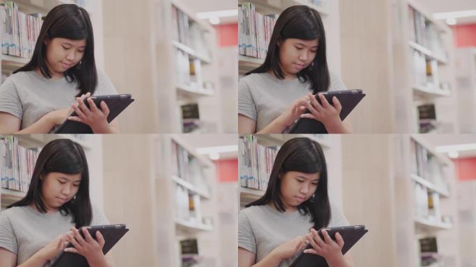 图书馆里的亚洲小女孩拿着平板电脑在互联网上搜索信息。技术和概念教育