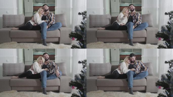 快乐的高加索丈夫和妻子坐在沙发上拥抱的肖像。恋爱中的情侣一起在家度过周末。休闲，休息，结合。