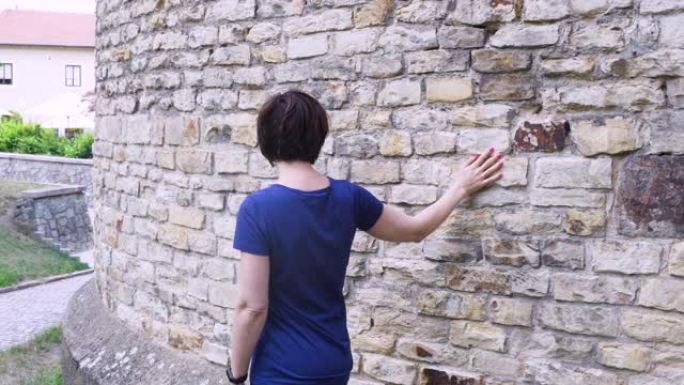 女人用手滑向古老的石墙。在古老美丽的欧洲城市中，女性的手触摸坚硬的岩石表面。感性的触摸。坚硬的石头表