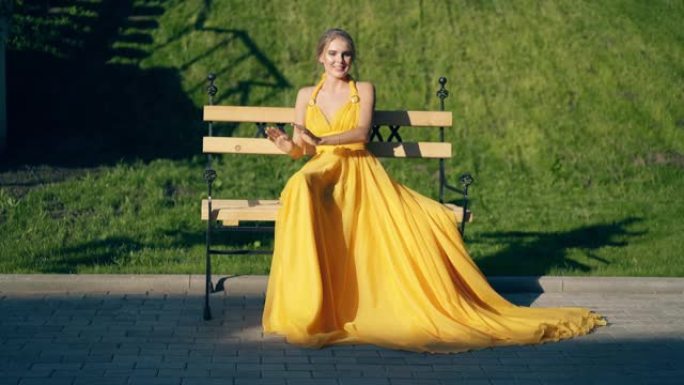 年轻漂亮的女孩穿着漂亮的黄色晚礼服，坐在长凳上