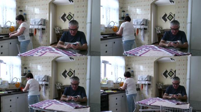 已婚老年夫妇在厨房，丈夫在厨房看手机，妻子在厨房水槽