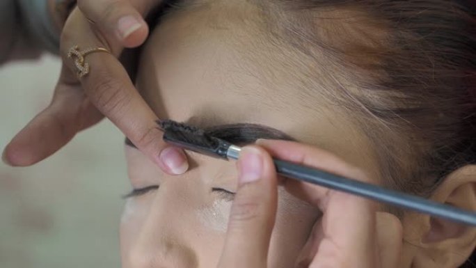 眉毛化妆，专业化妆师用特殊的眉刷梳理模特眉毛，特写，微距