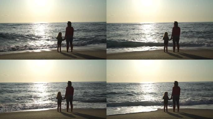 日落时和妈妈站在海滩上的小女孩