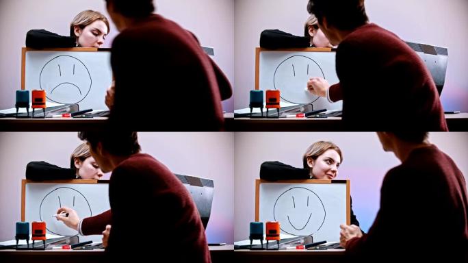 办公室工作-一个男人来到一个女人面前，在铭牌上有一个悲伤的笑脸-擦除标志并画一个笑脸
