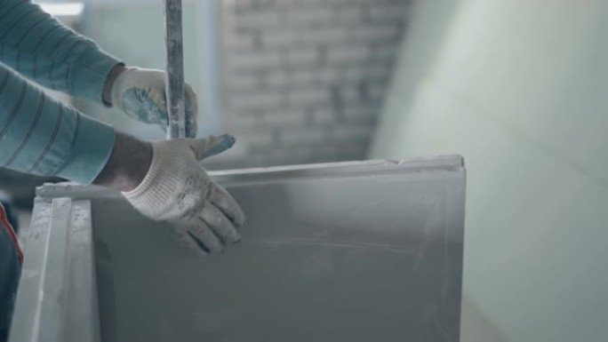 戴手套的熟练画家测量白色石膏石膏板