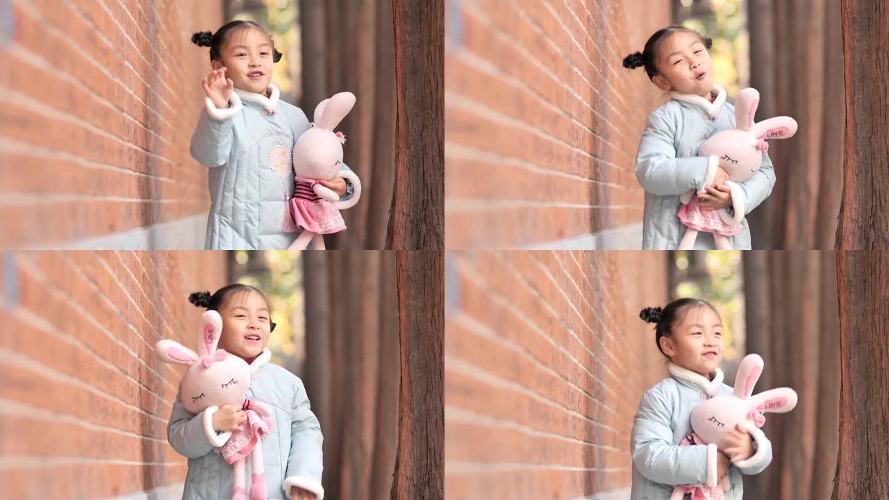 穿着蓝色新年衣服的快乐中国女孩带着她最喜欢的兔子玩具在户外跳舞，4-5岁，非常可爱，4k镜头，慢动作