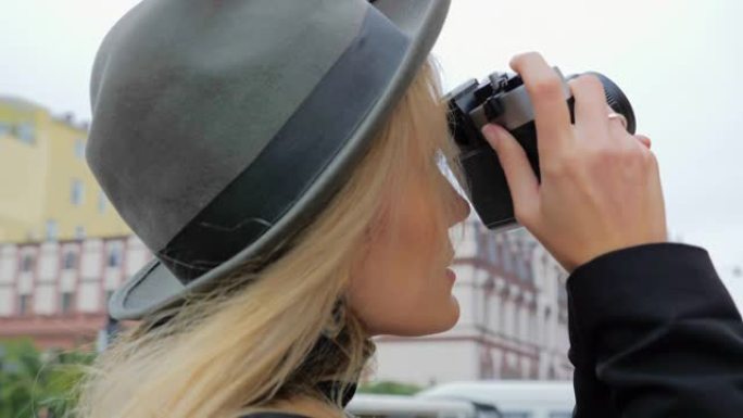 一位年轻的白人妇女，一位戴着帽子的潮人在一台老式电影相机上拍照。工作中的印刷版概念记者博客