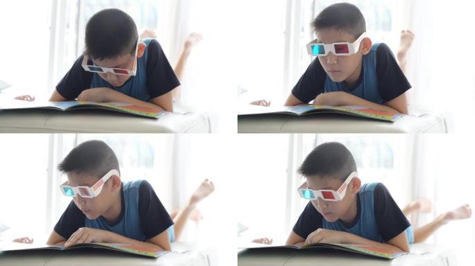 亚洲男孩躺在床上，戴着3d眼镜，在家窗户附近看书。