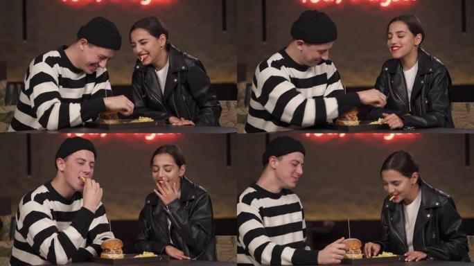 情侣在时尚的室内城市餐厅约会。年轻人正在吃炸薯条，一起享受他们的晚餐。恋爱中的人