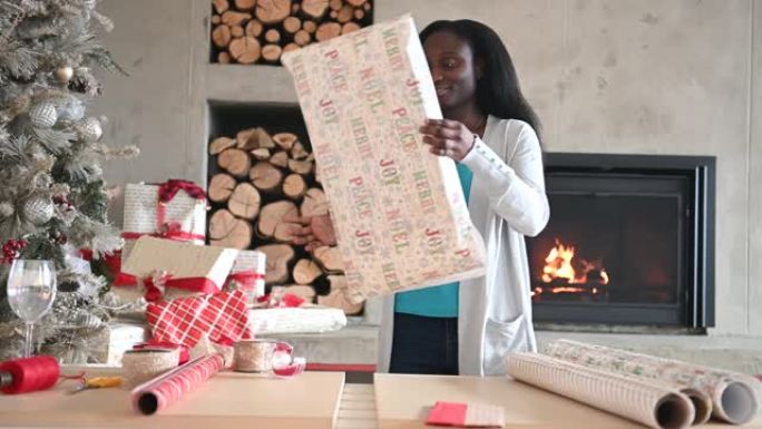 美国黑人年轻女子独自在壁炉和圣诞树旁包裹圣诞礼物