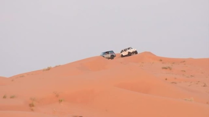 在阿拉伯联合酋长国Ras al Khaimah的傍晚日落时分，汽车和吉普车驶过橙色沙丘。沙丘扑打和娱